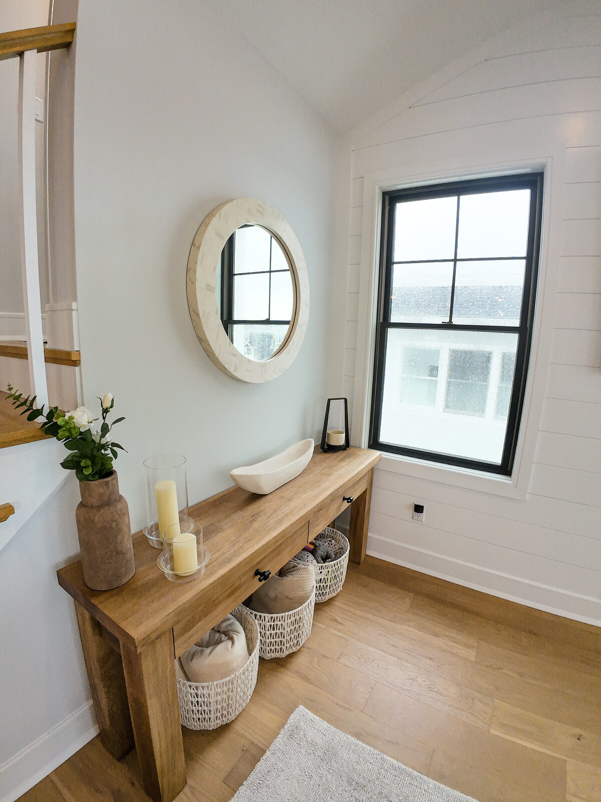Entry console in white oak with woven baskets, candles, and a round bone inlay mirror