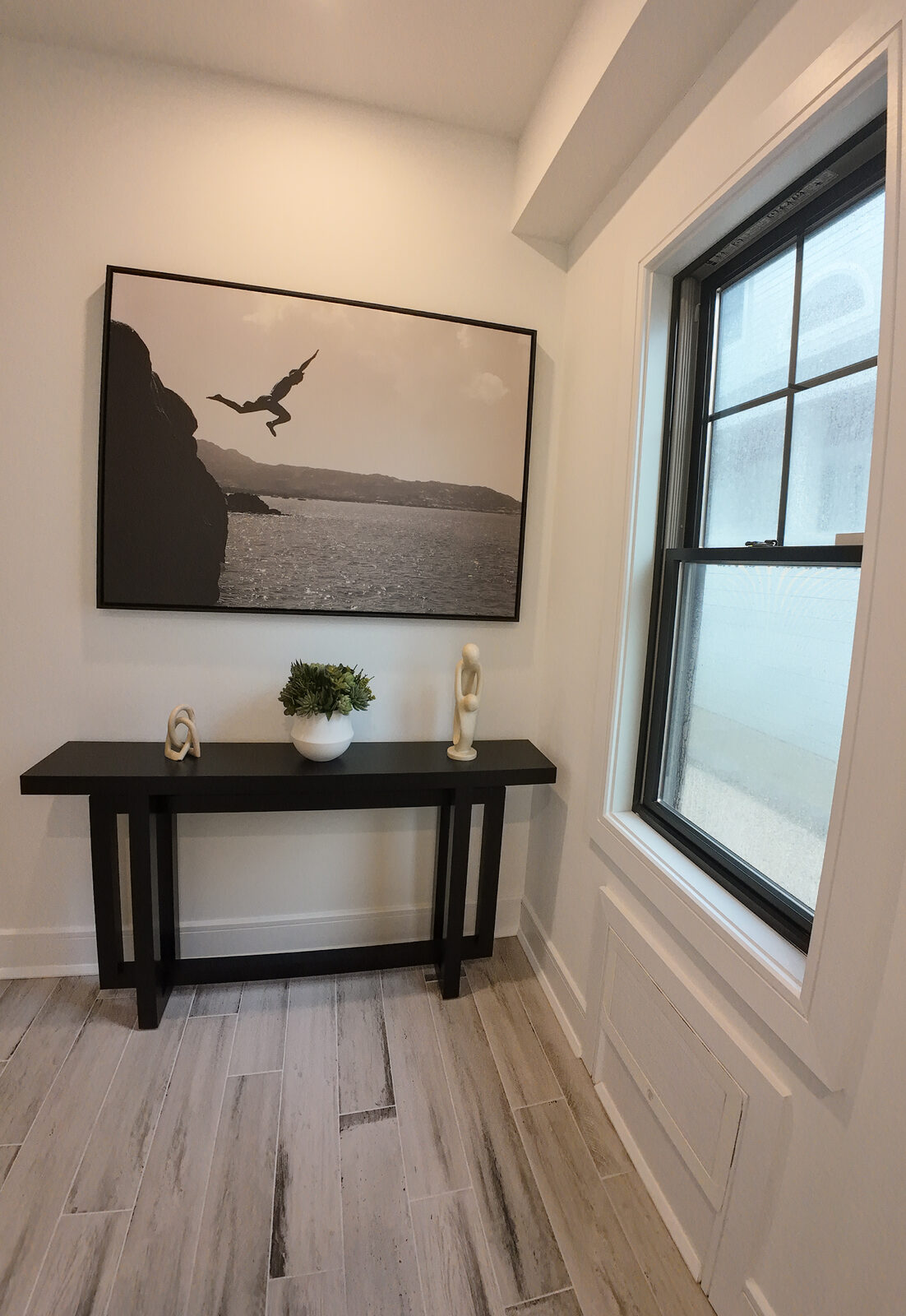 Hallway vignette with black console table, sculptural objects, and large black and white cliff diving photograph
