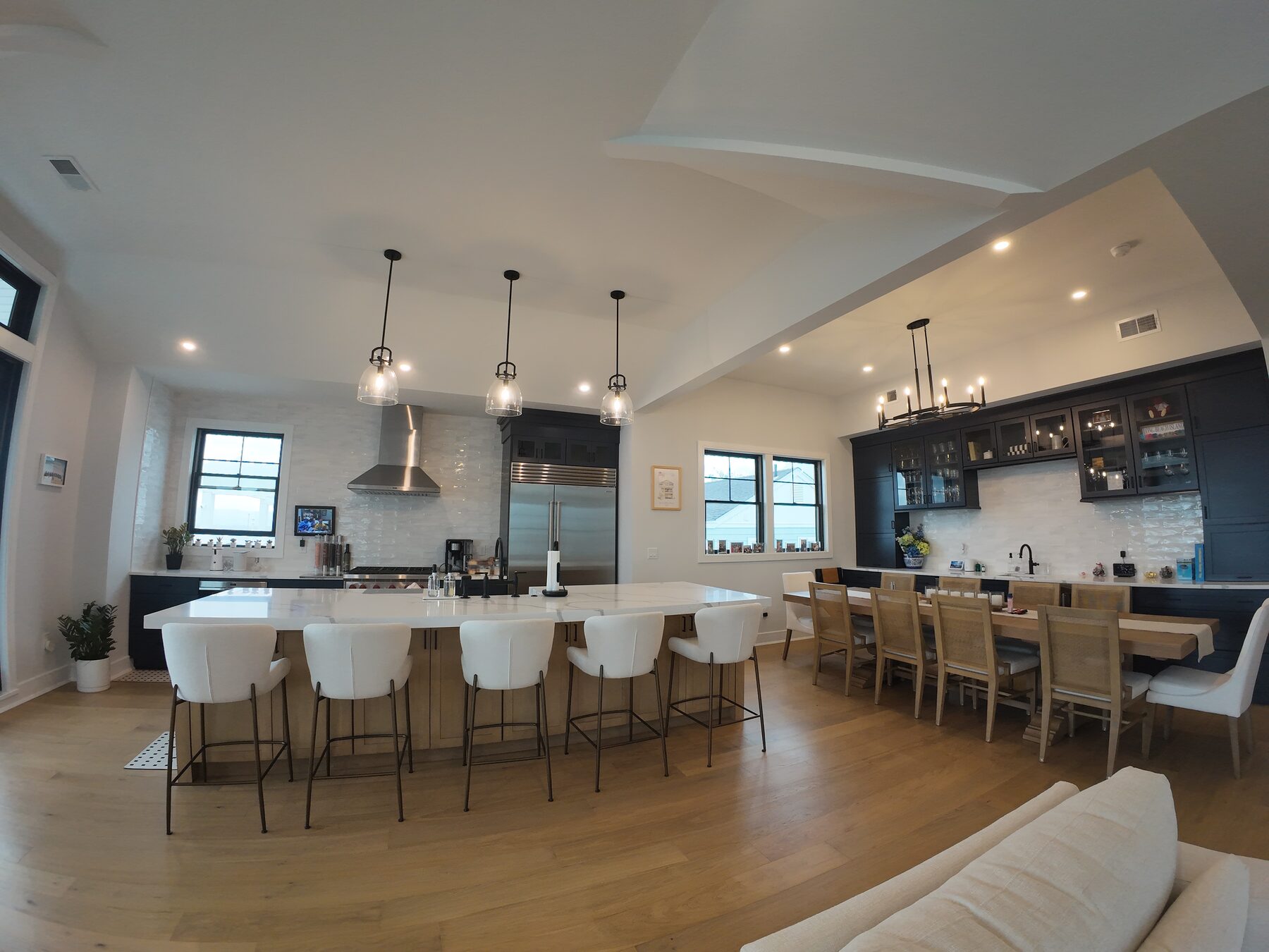 Open plan kitchen and dining space with white oak floors, oversized quartz island, and dark bar cabinetry