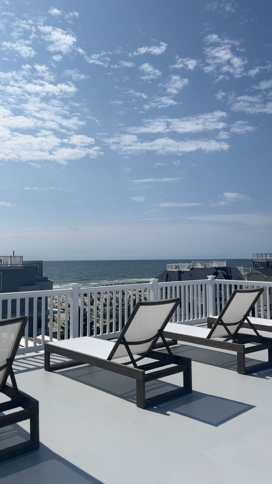 Rooftop deck with sling lounge chairs, white railing, and ocean views over the dunes