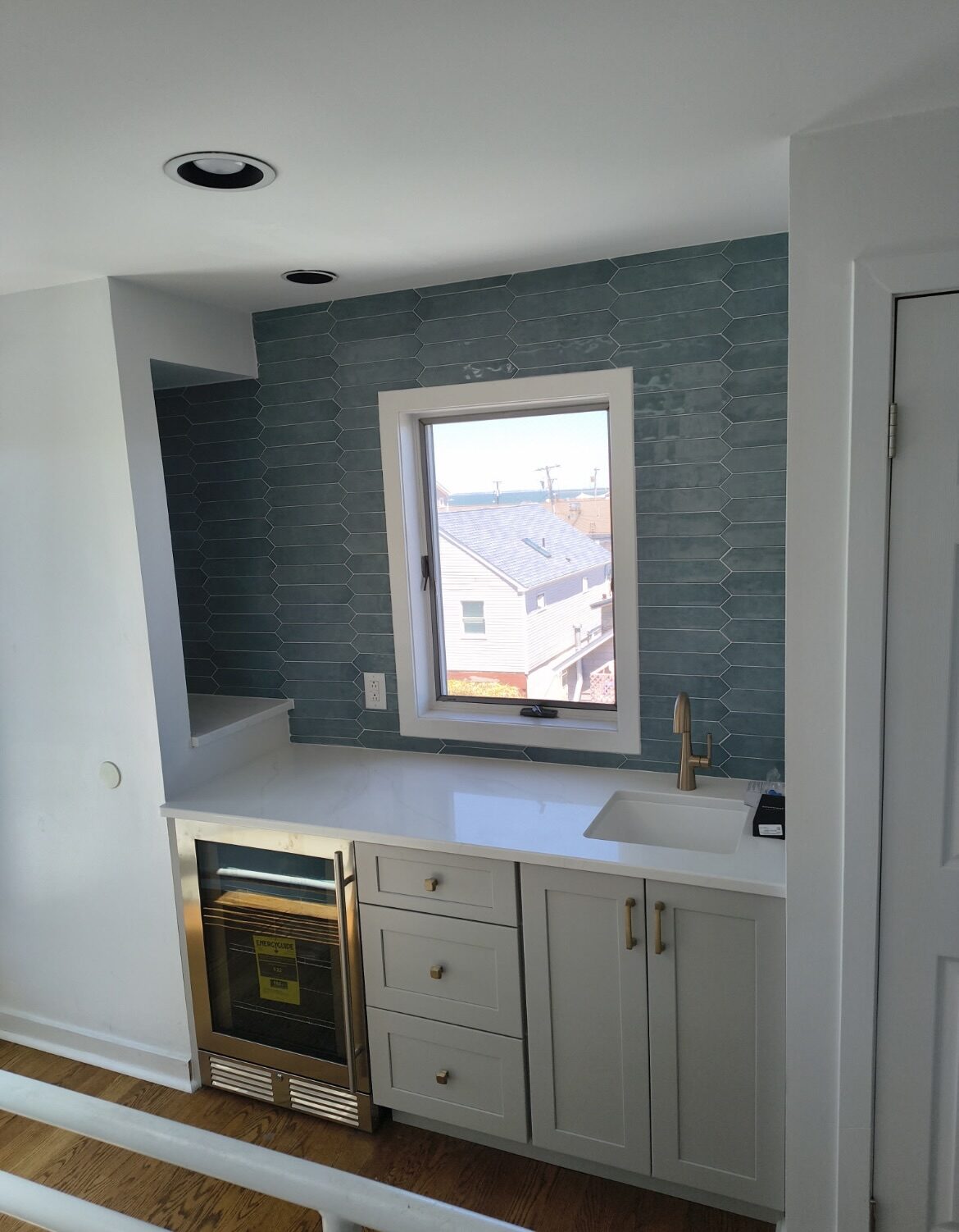 Wet bar with blue picket tile wall, white quartz counter, brass hardware, and beverage fridge